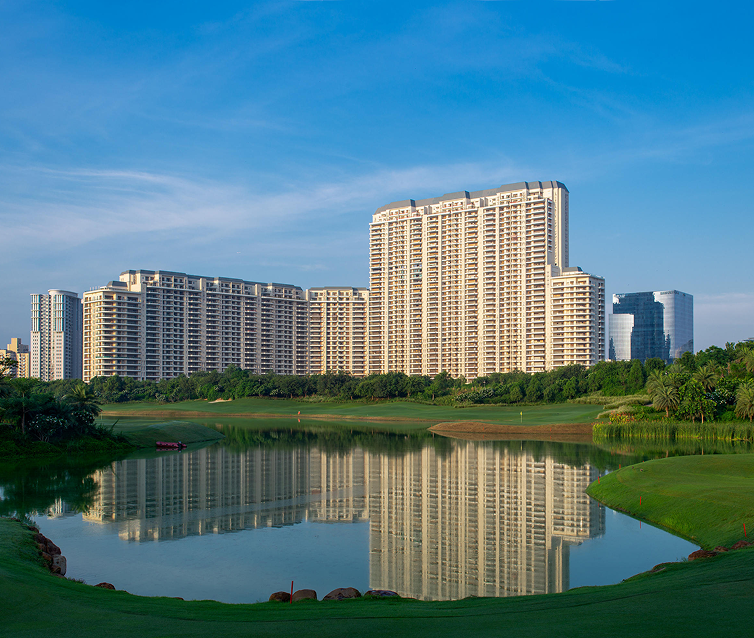 Large residential building complex with lake and green grass in front, under blue sky